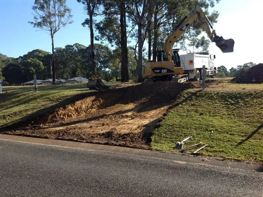 A Cat Excavator is Moving Dirt on the Side of a Road — S M & A J Gilbert Earthmoving in Mitchells Island, NSW