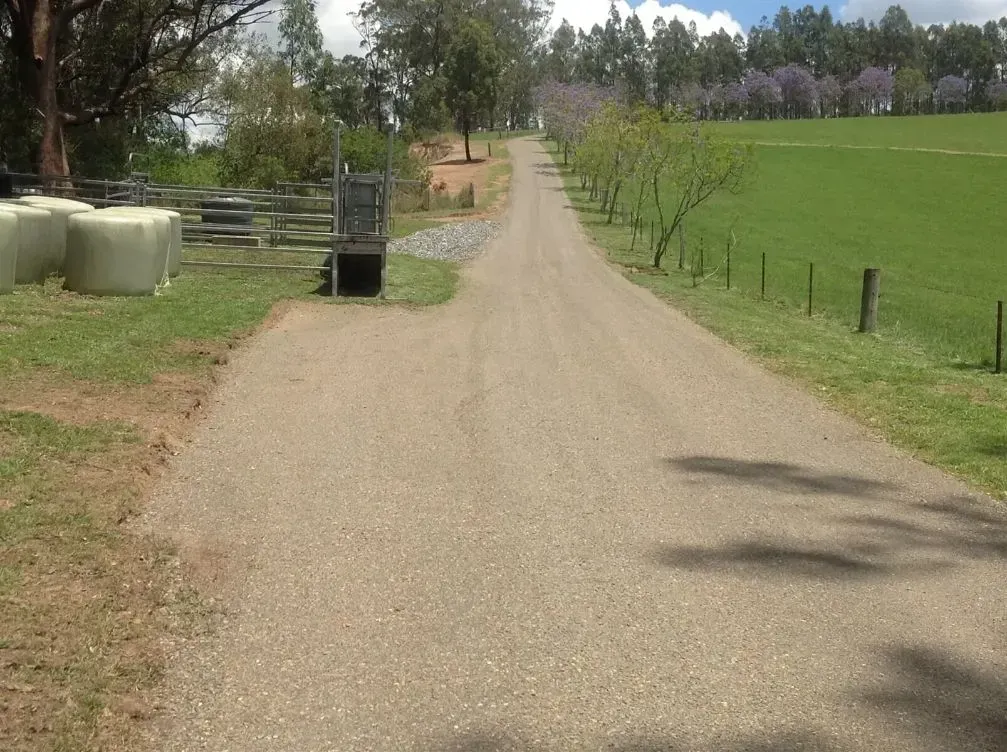 A Dirt Road Going Through a Grassy Field With Fence — S M & A J Gilbert Earthmoving in Mitchells Island, NSW