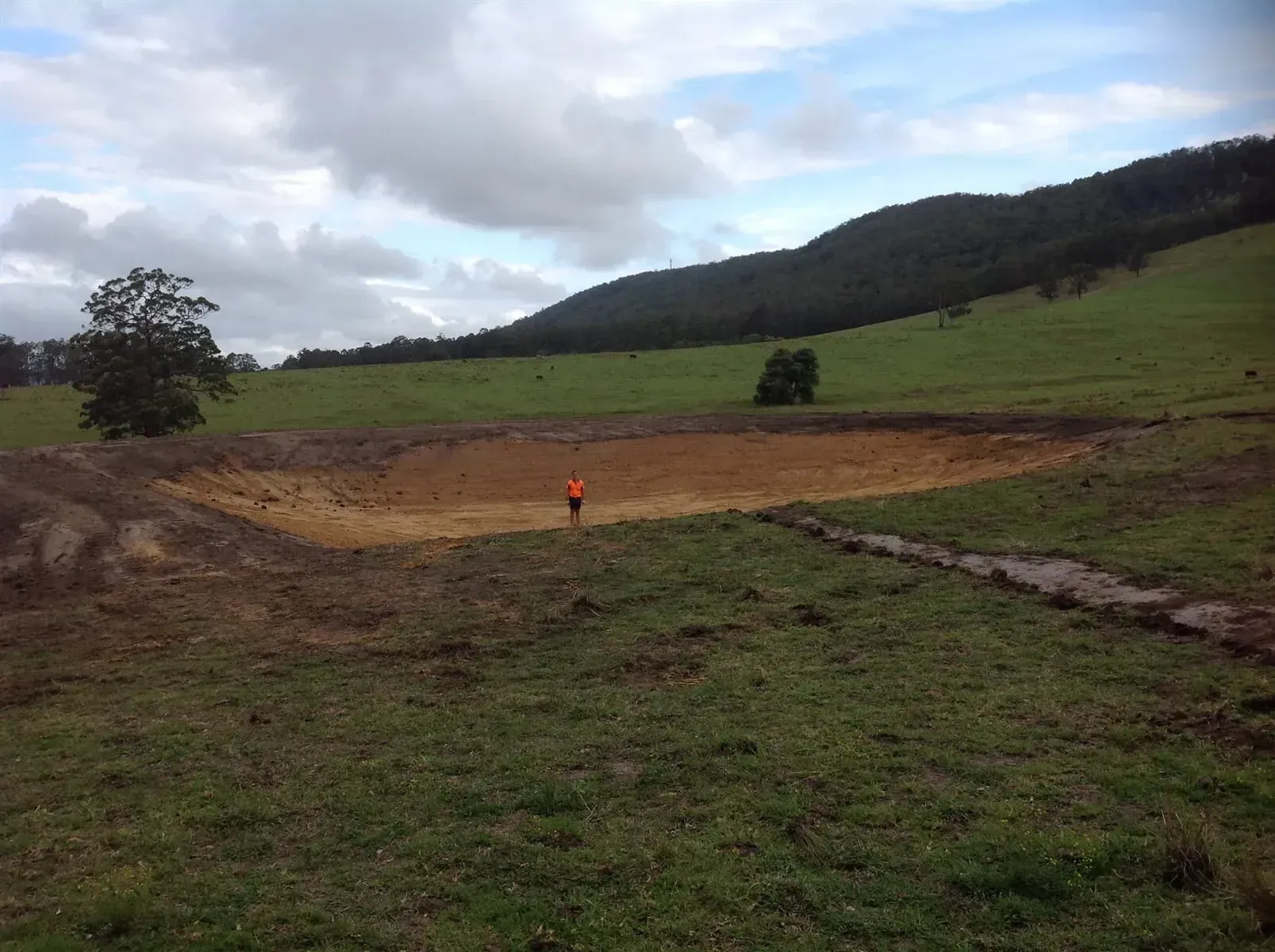 A Man in an Orange Vest is Standing in the Middle of a Crater — S M & A J Gilbert Earthmoving in Mitchells Island, NSW