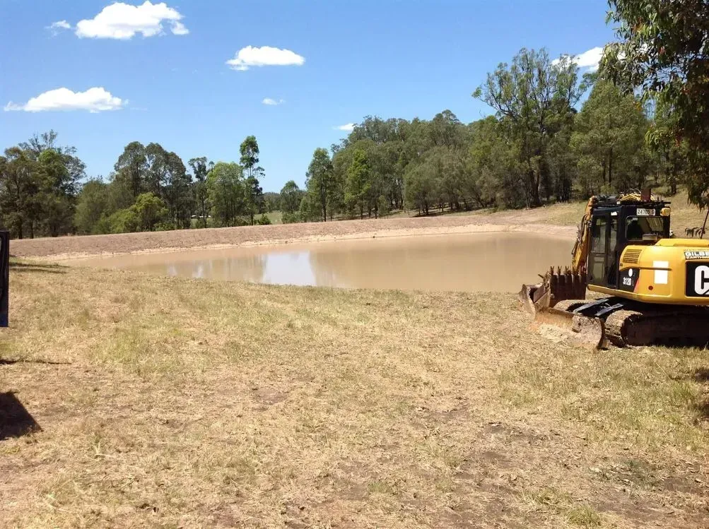 A Yellow Excavator With the Letter C on the Side of It In A While Field — S M & A J Gilbert Earthmoving in Mitchells Island, NSW