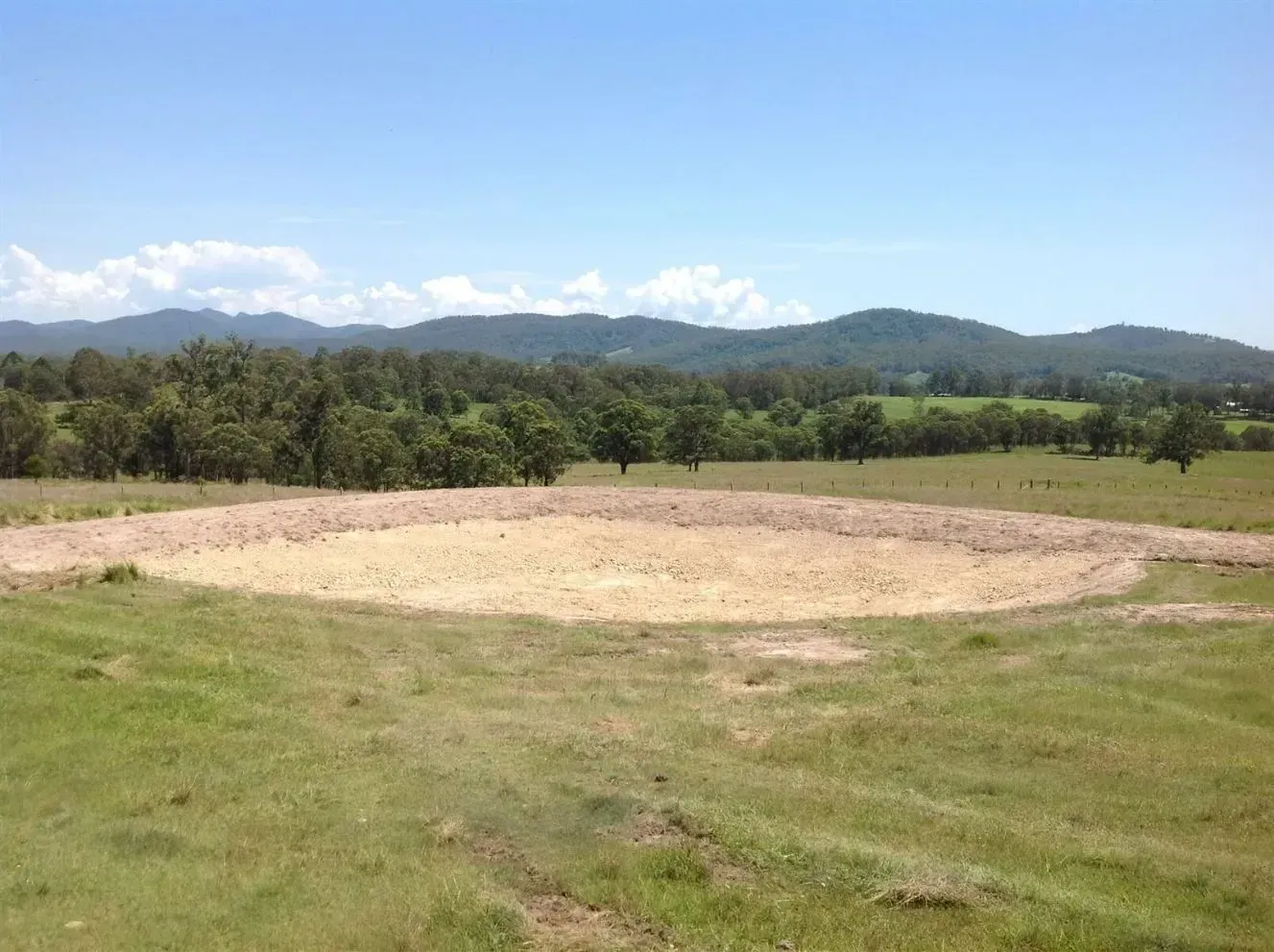 An Empty, Circular Dam on a Grassy Field, With Hills and Trees — S M & A J Gilbert Earthmoving in Mitchells Island, NSW