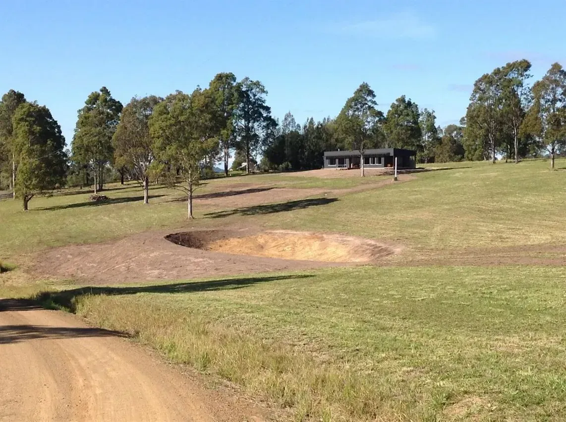 A Long Dirt Road Going Through a Grassy Field With a House in the Background — S M & A J Gilbert Earthmoving in Mitchells Island, NSW