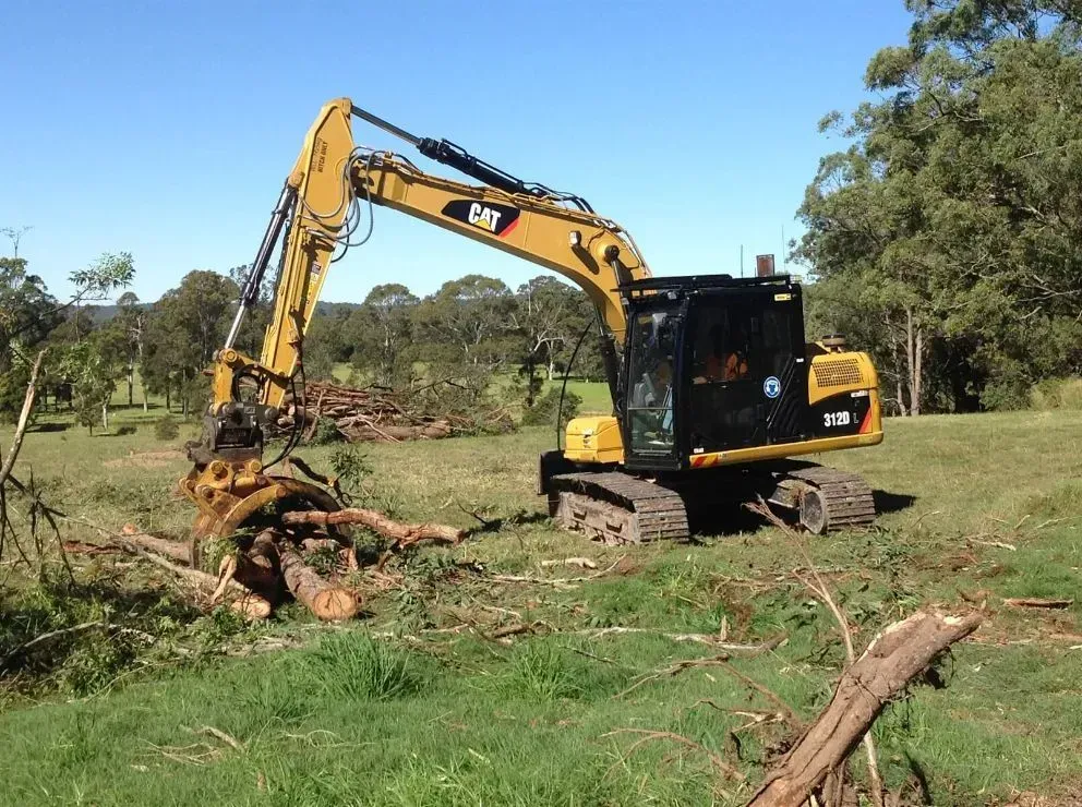 A Cat Excavator is Cutting Down Big Log in a Field — S M & A J Gilbert Earthmoving in Mitchells Island, NSW