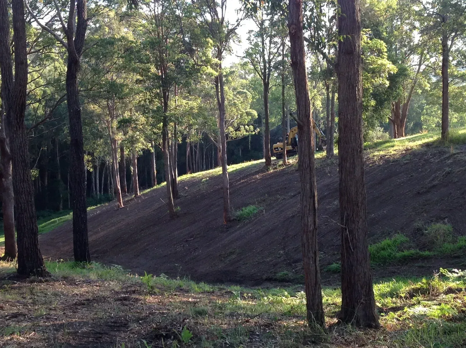 A Tractor is Driving Down a Hill in the Woods At A Slow Pace — S M & A J Gilbert Earthmoving in Mitchells Island, NSW