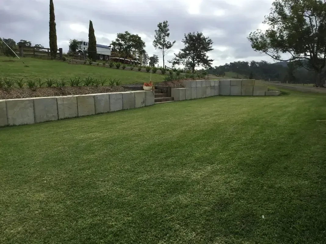 A Lush Green Lawn With a Stone Walls in the Background — S M & A J Gilbert Earthmoving in Mitchells Island, NSW