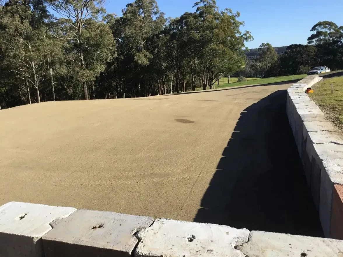 A Concrete Wall Surrounds a Dirt Field With Forest — S M & A J Gilbert Earthmoving in Mitchells Island, NSW