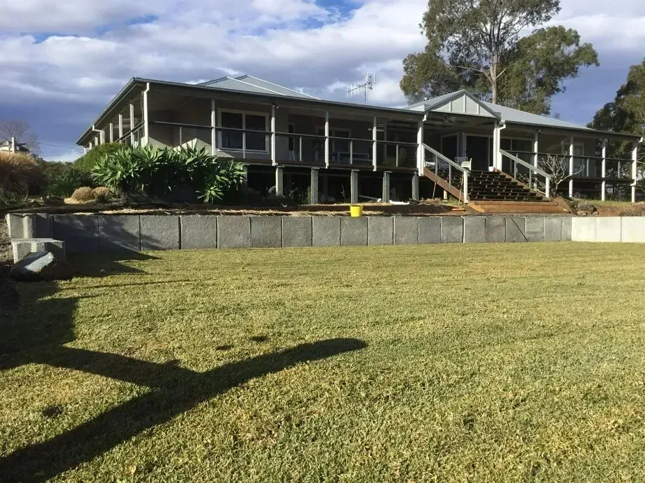 A Large House With a Large Lawn And Stone Walls in Front of It — S M & A J Gilbert Earthmoving in Mitchells Island, NSW