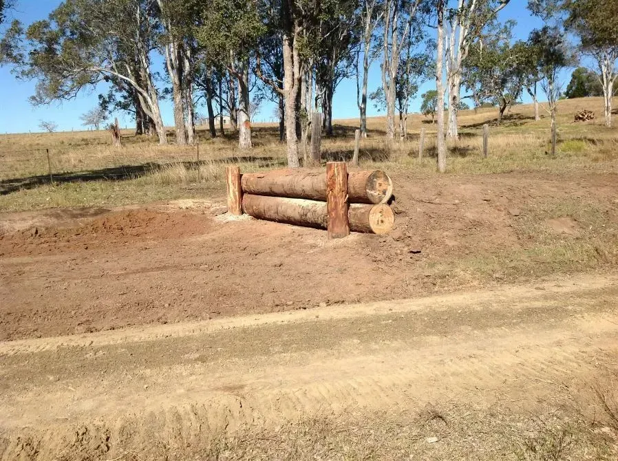 A Fence Made of Logs in a Field With Trees in the Background — S M & A J Gilbert Earthmoving in Mitchells Island, NSW