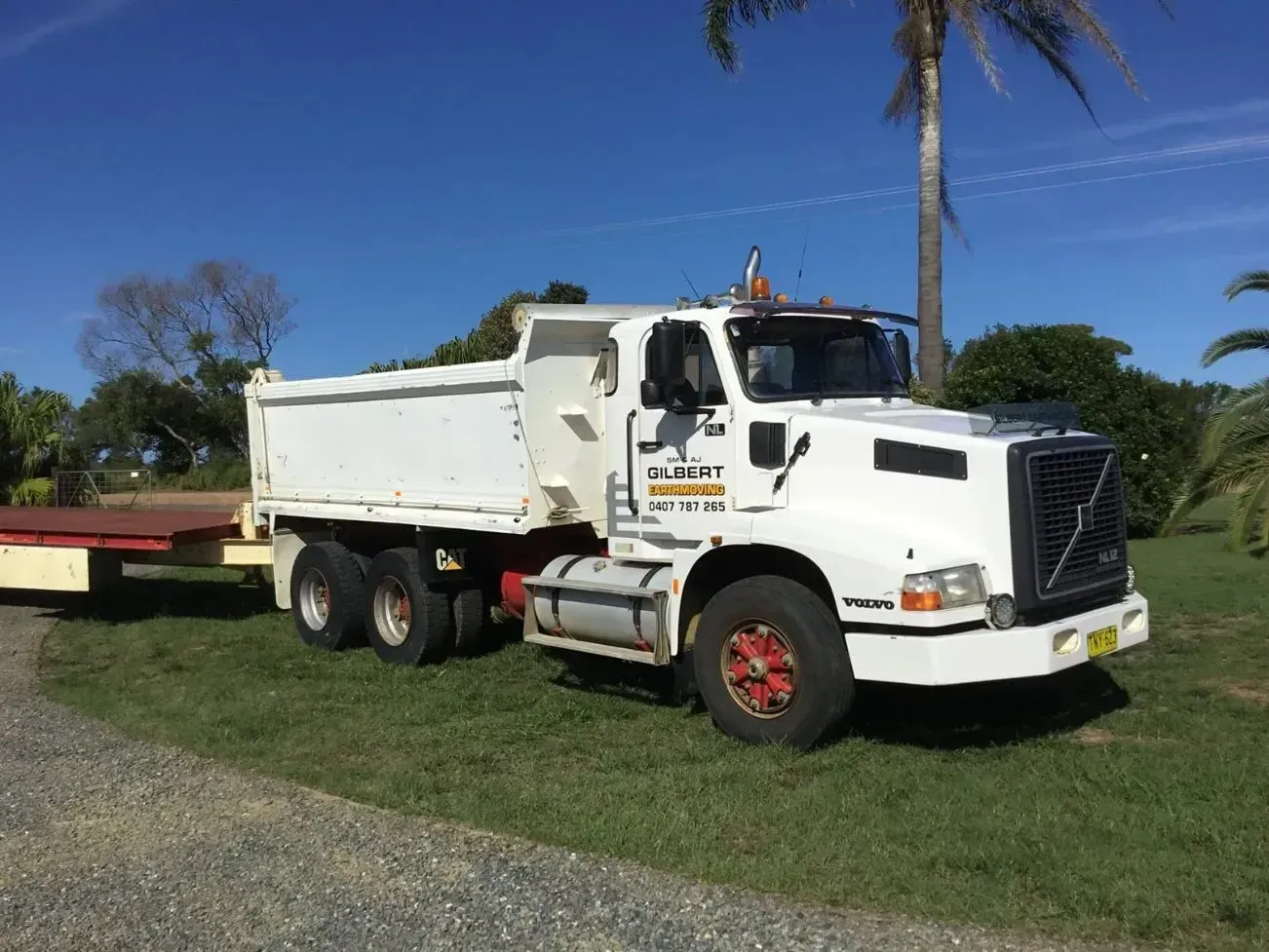 A White Dump Truck With a Trailer Attached to It is Parked in a Grassy Field — S M & A J Gilbert Earthmoving in Mitchells Island, NSW