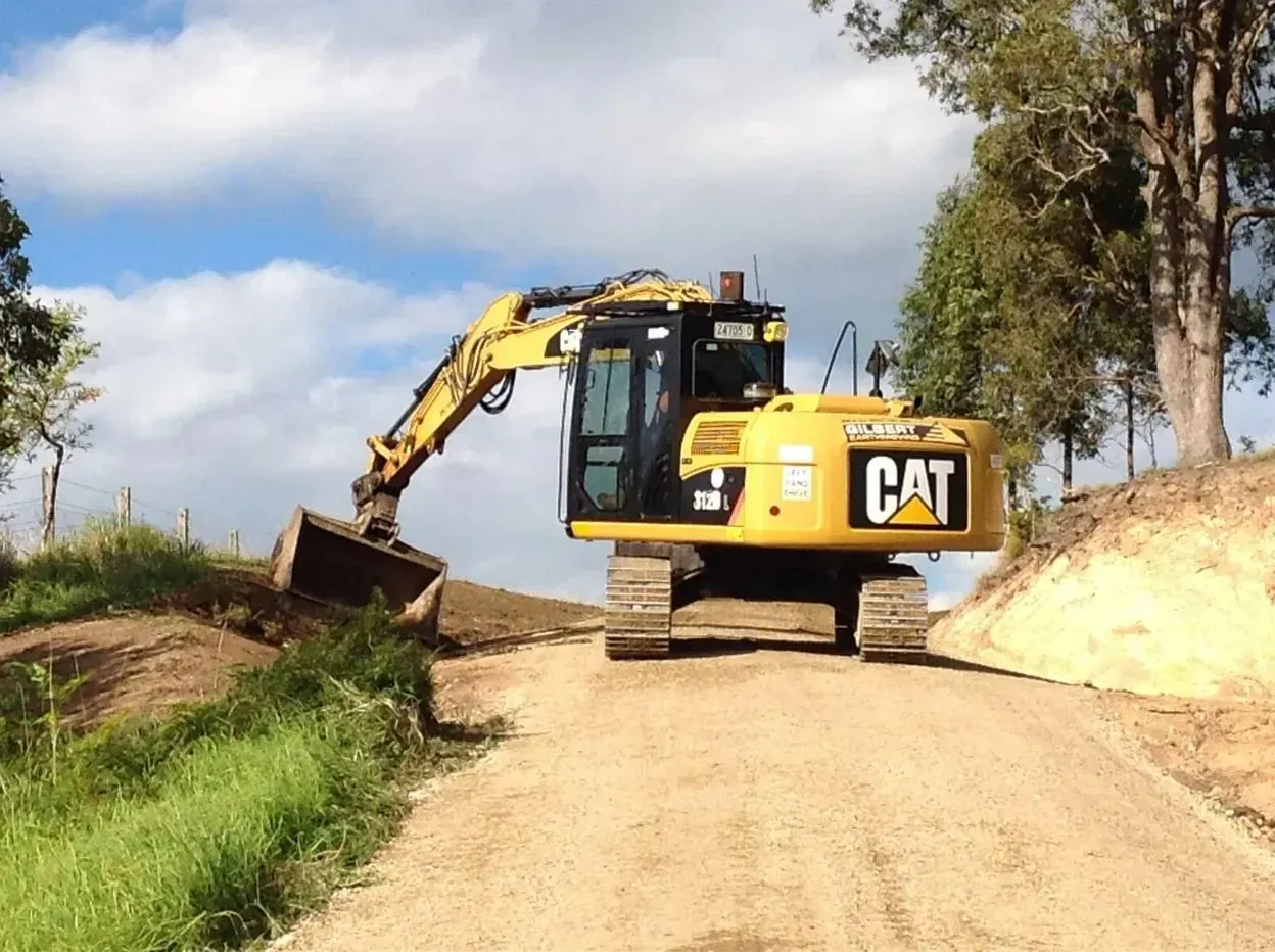 A Yellow Cat Excavator is Driving Down a White Sand Road — S M & A J Gilbert Earthmoving in Mitchells Island, NSW