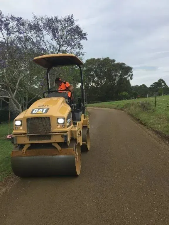 A Vertical Shot Of A Yellow Cat Roller is Driving Down a Dirt Road — S M & A J Gilbert Earthmoving in Mitchells Island, NSW