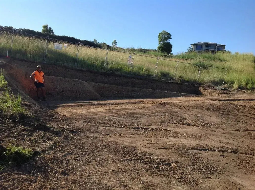 A Man in an Orange Vest is Walking Down a Dirt Hill — S M & A J Gilbert Earthmoving in Mitchells Island, NSW