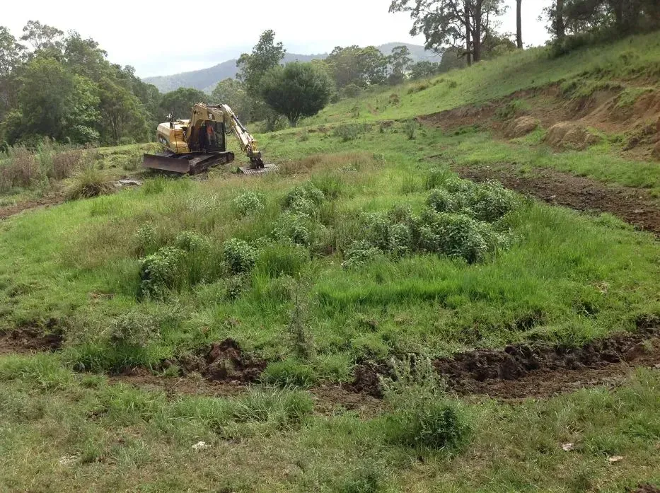 A Bulldozer is Sitting in the Middle of a Grassy And Muddy Field — S M & A J Gilbert Earthmoving in Mitchells Island, NSW