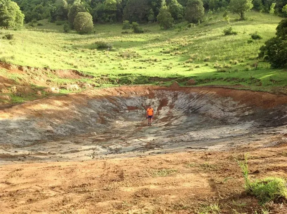 A Man With Orange Vest is Standing in the Middle of a Large Muddy Pond — S M & A J Gilbert Earthmoving in Mitchells Island, NSW