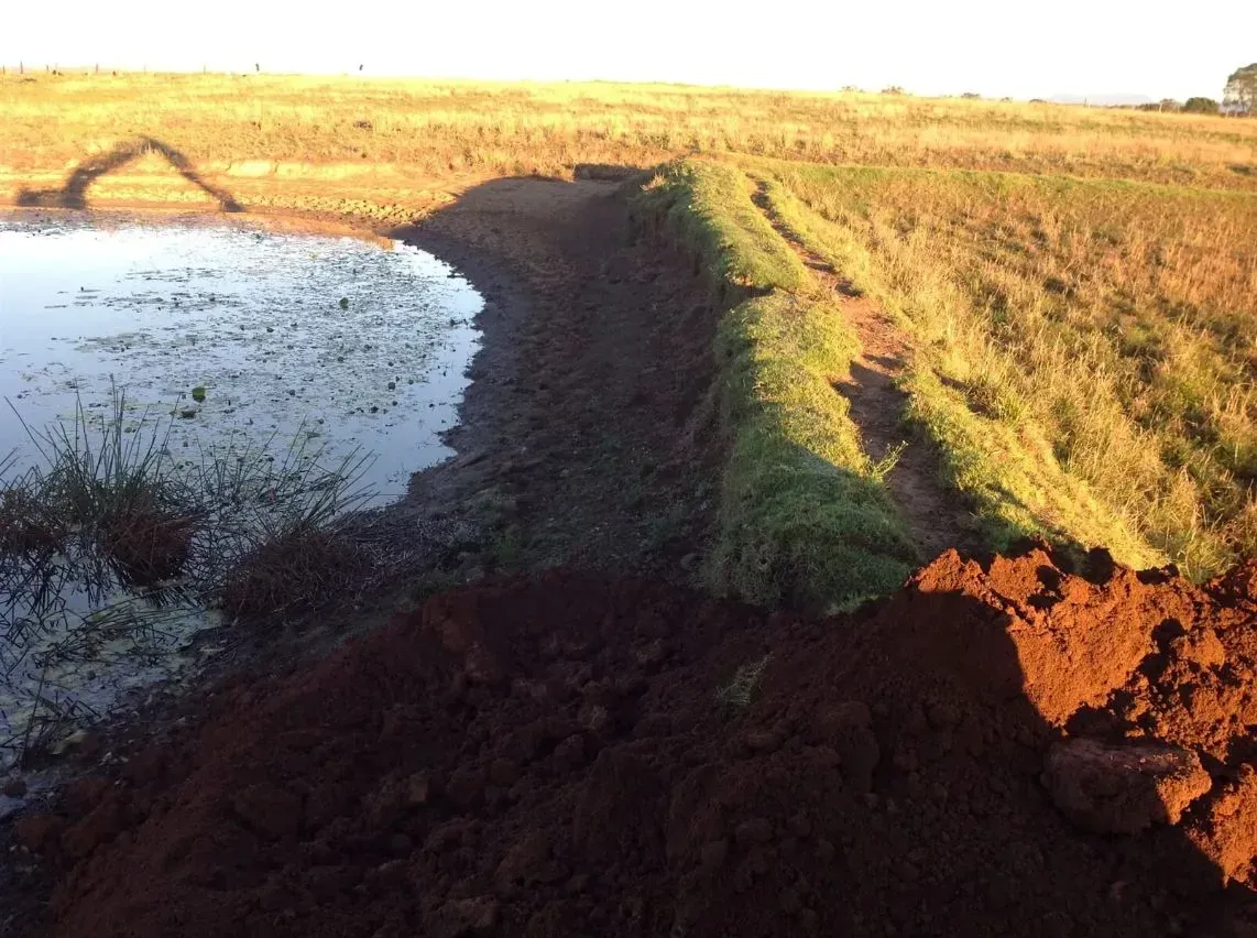 A Large Pile of Dirt is Sitting Next to a Body of Water in a Field — S M & A J Gilbert Earthmoving in Mitchells Island, NSW