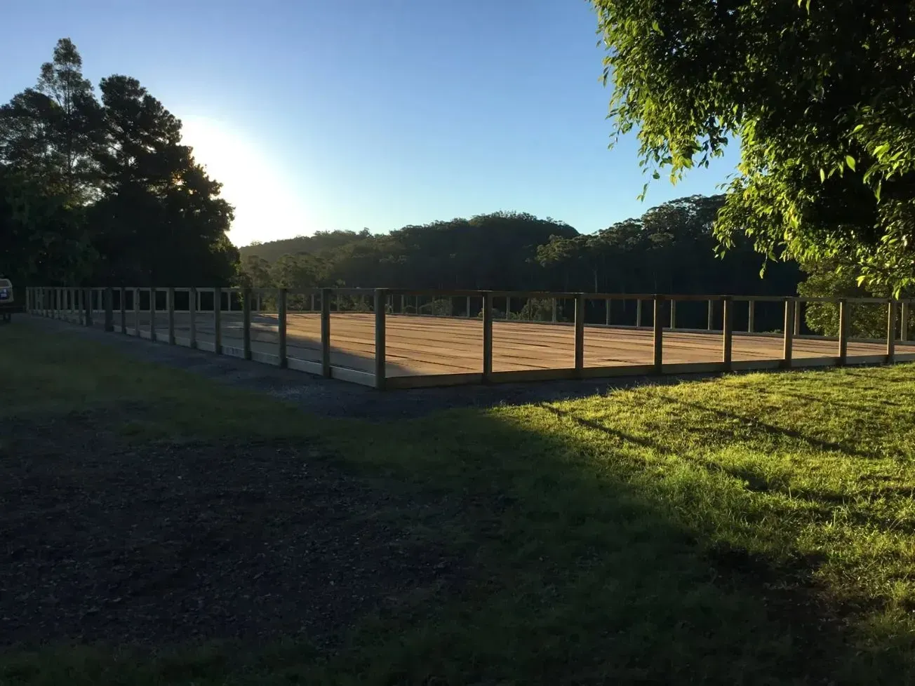 A Wooden Fence Surrounds a Grassy Field With Large Shadow — S M & A J Gilbert Earthmoving in Mitchells Island, NSW
