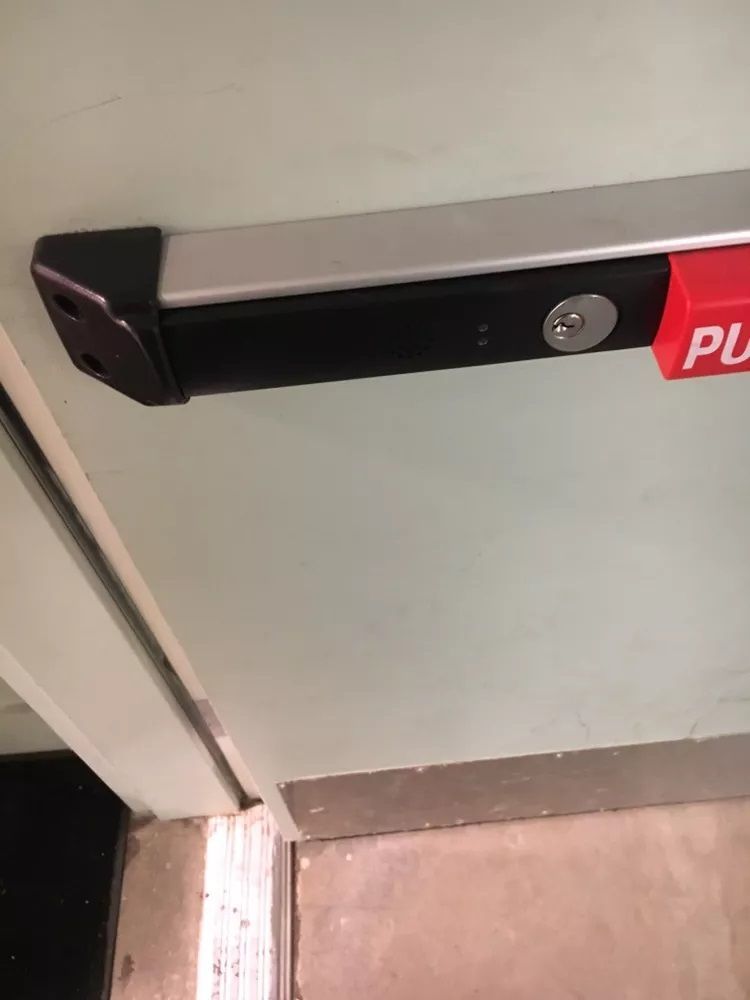 A close up of a door with a red push bar on it.