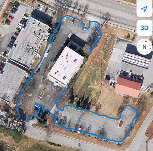 Aerial view of a commercial building with parking, outlined in blue. Surrounding land is partially developed.