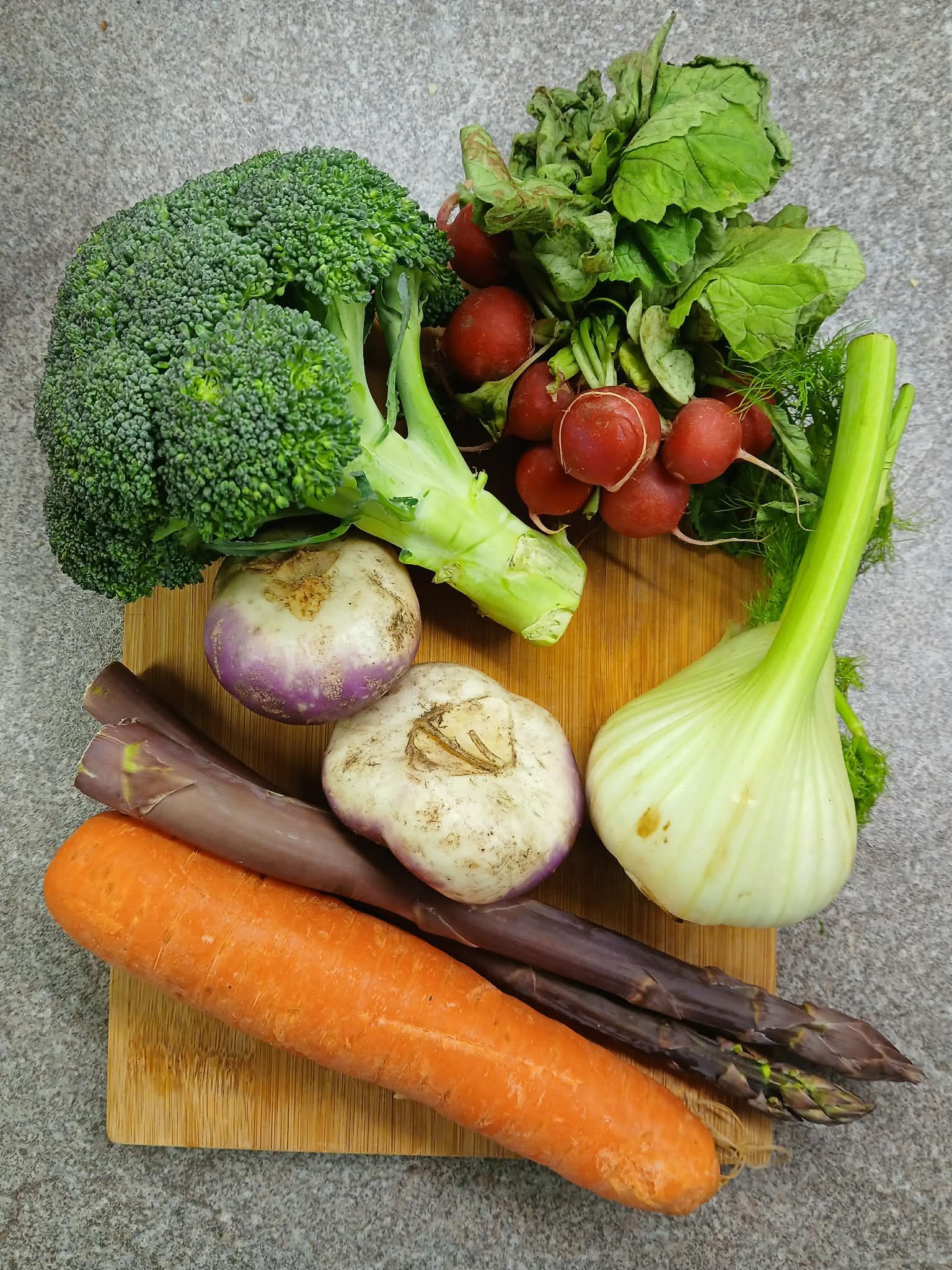 Assorted fresh vegetables on a cutting board, including broccoli, tomatoes, fennel, carrots, and potatoes.