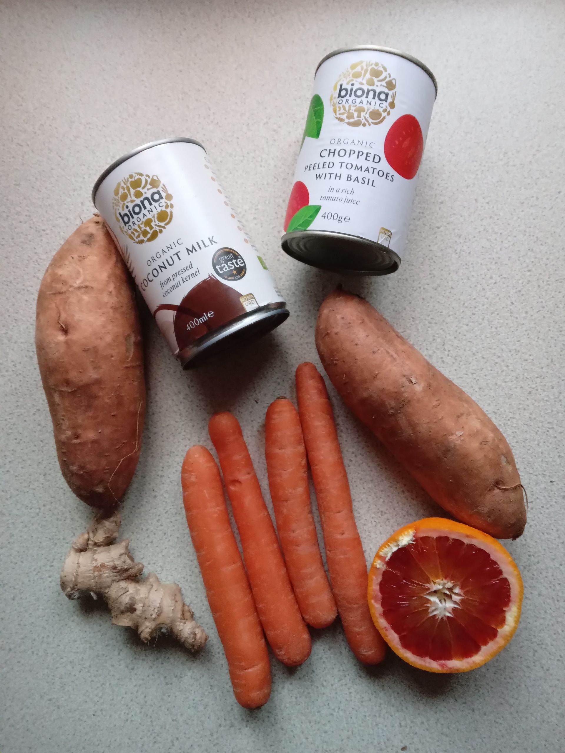 Sweet potatoes, carrots, ginger, blood orange, and two cans arranged on a white background.
