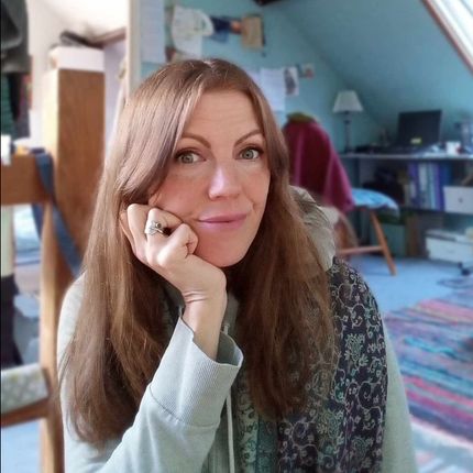 Woman resting her chin on her hand in a cozy room with blue walls and a patterned rug.
