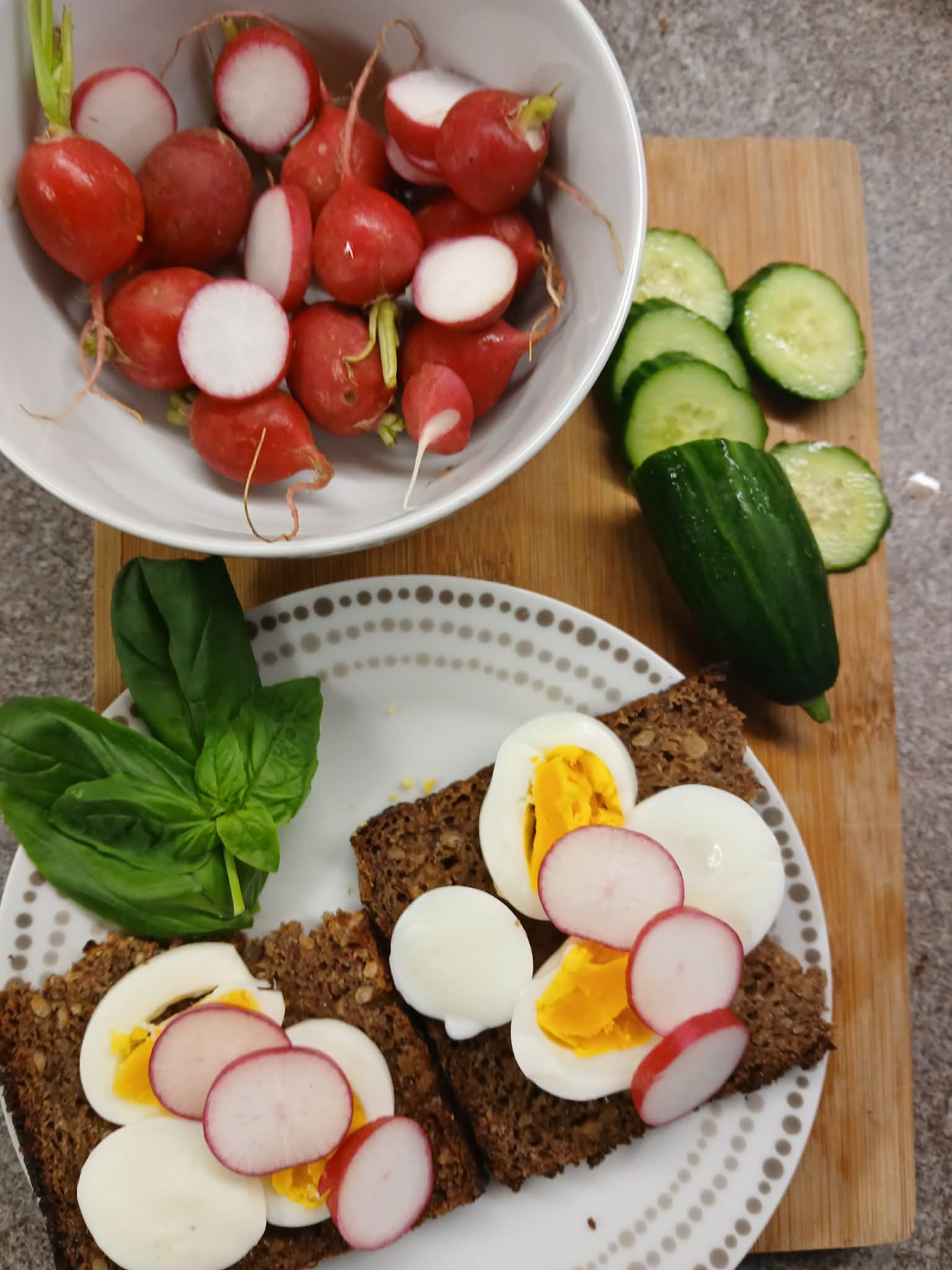 Radishes, cucumber slices, basil, and rye bread topped with sliced boiled eggs on a plate