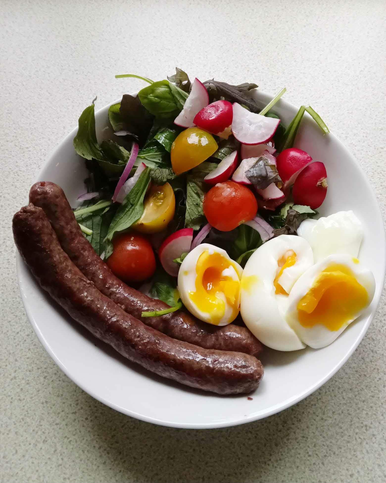 Plate with grilled sausages, salad greens and cherry tomatoes, plus two soft-boiled eggs with runny yolks