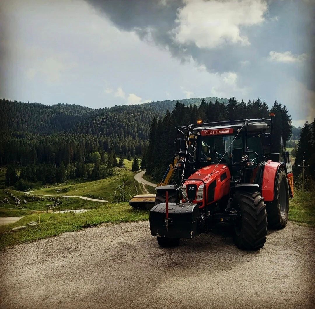 Trattore rosso parcheggiato su una strada sterrata, con vista su una montagna ricoperta di foresta sotto un cielo nuvoloso.