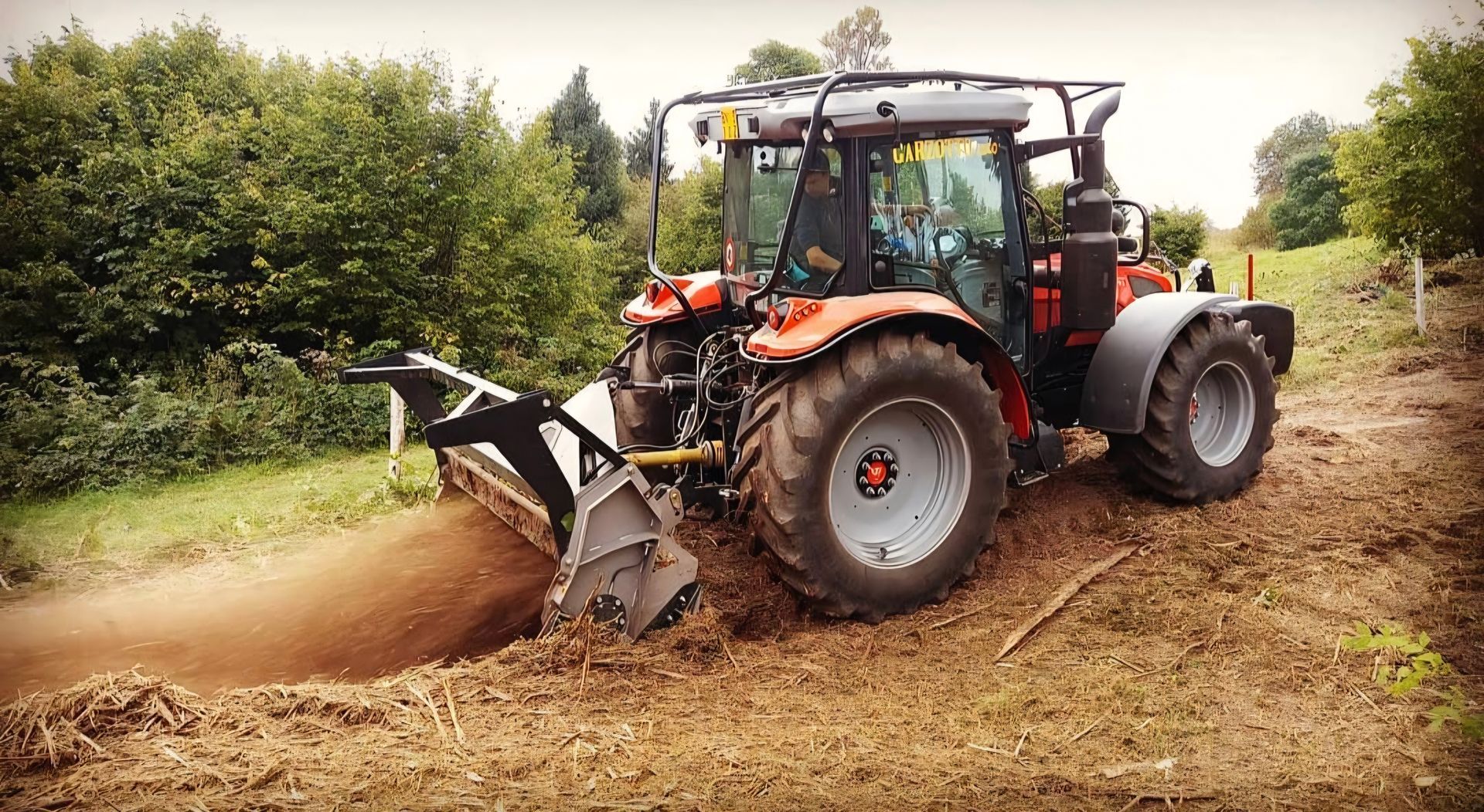 Trattore arancione con motocoltivatore che coltiva il terreno in un campo.