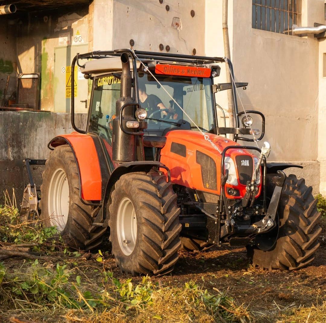 Trattore arancione parcheggiato vicino a un edificio di cemento; giorno.