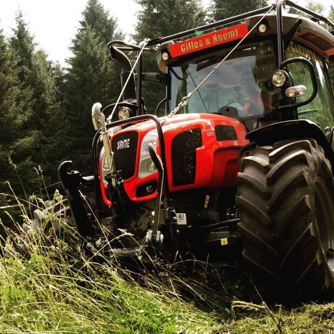 Trattore rosso in una radura della foresta, con alberi alti sullo sfondo.