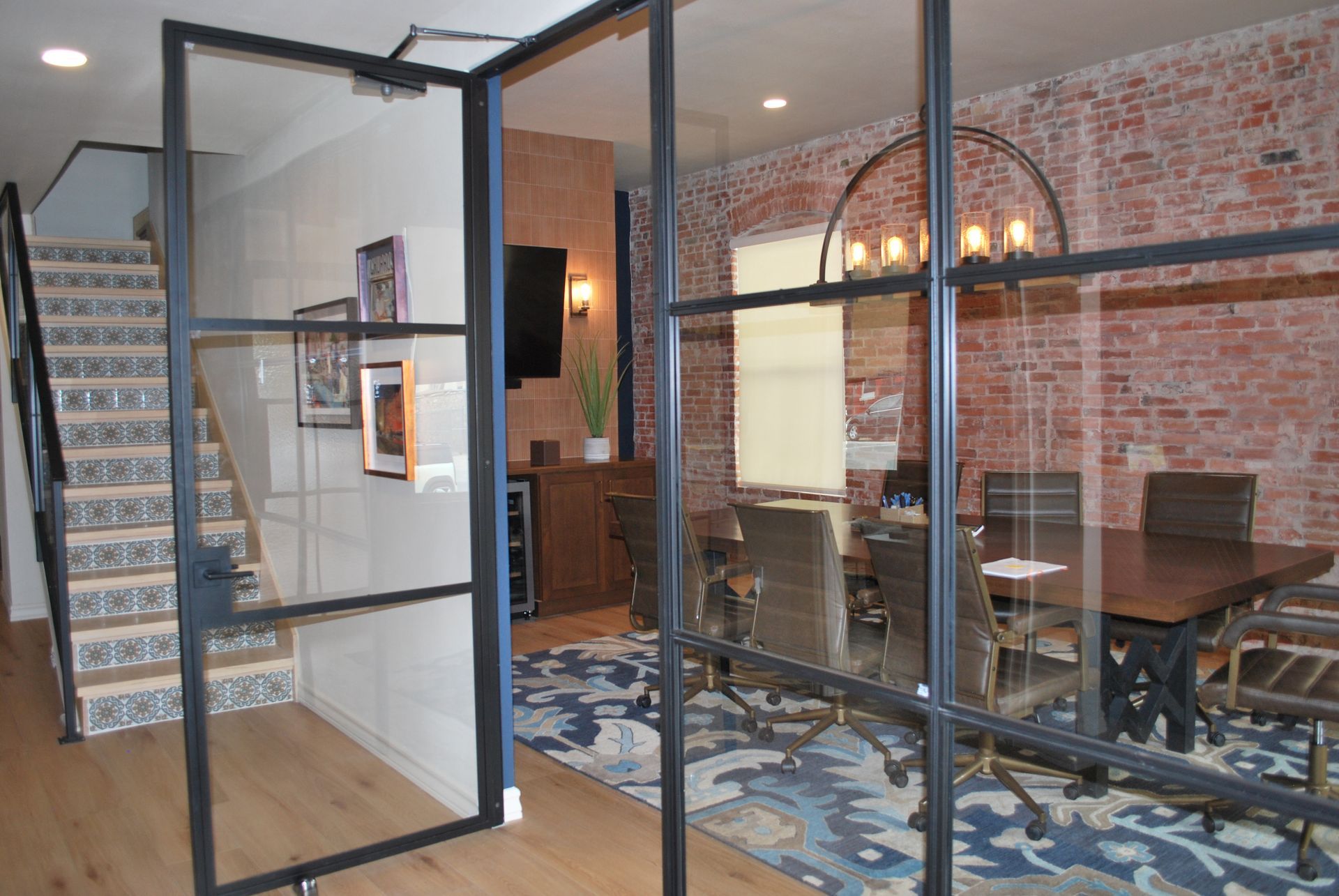 Glass-walled office with conference table, exposed brick, and stairs.