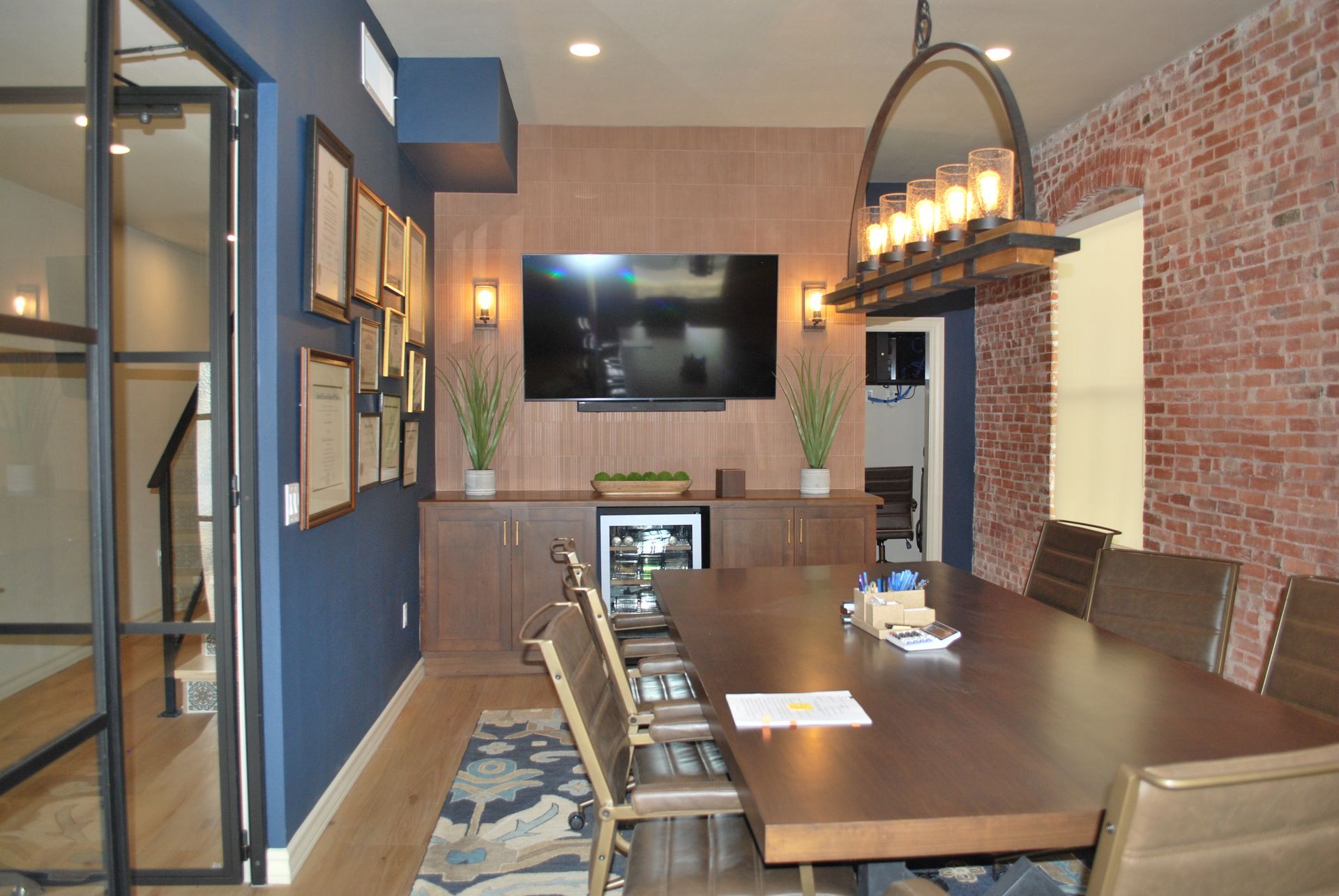 Modern dining room with a long table, TV, exposed brick wall, and a large mirror.