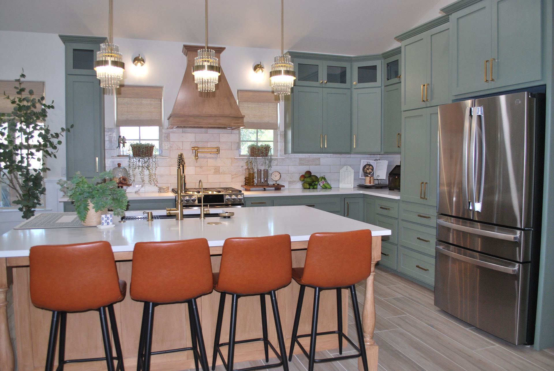 Kitchen with green cabinets, a large island with orange stools, and stainless steel refrigerator.