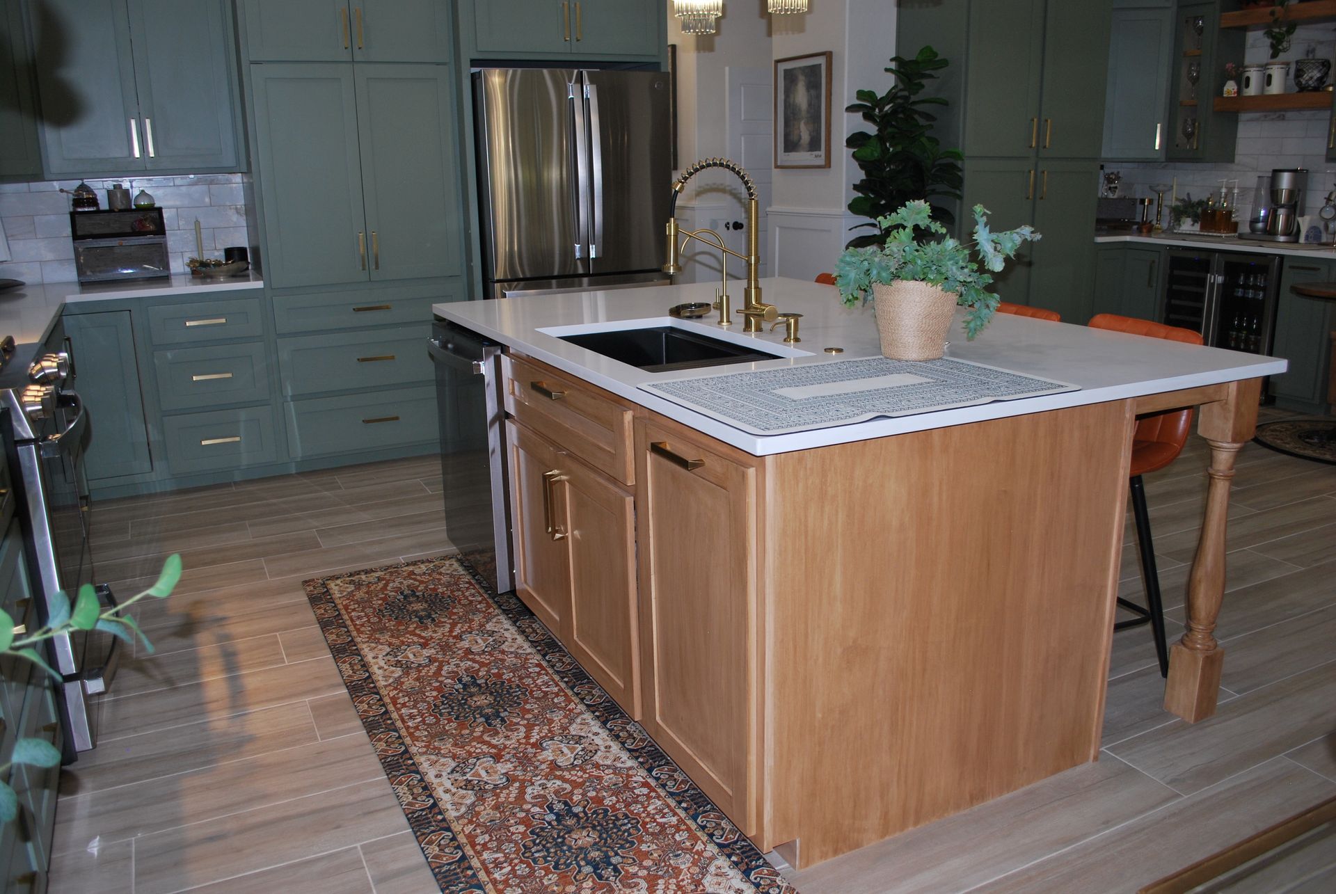 Kitchen with green cabinets, stainless steel appliances, and a light wood island with a sink and gold faucet.
