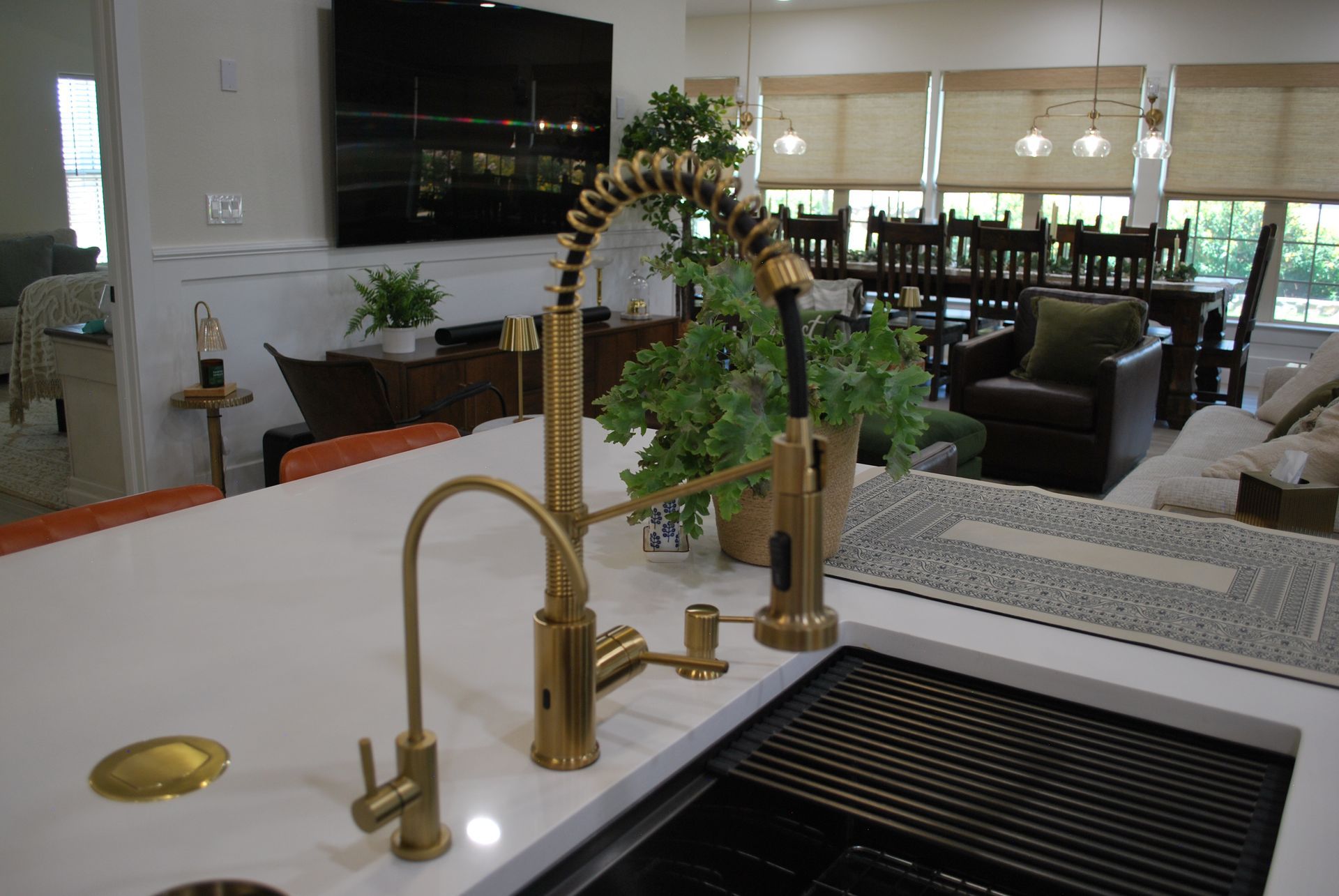 Gold kitchen faucet on white countertop, with sink and dining area in background.