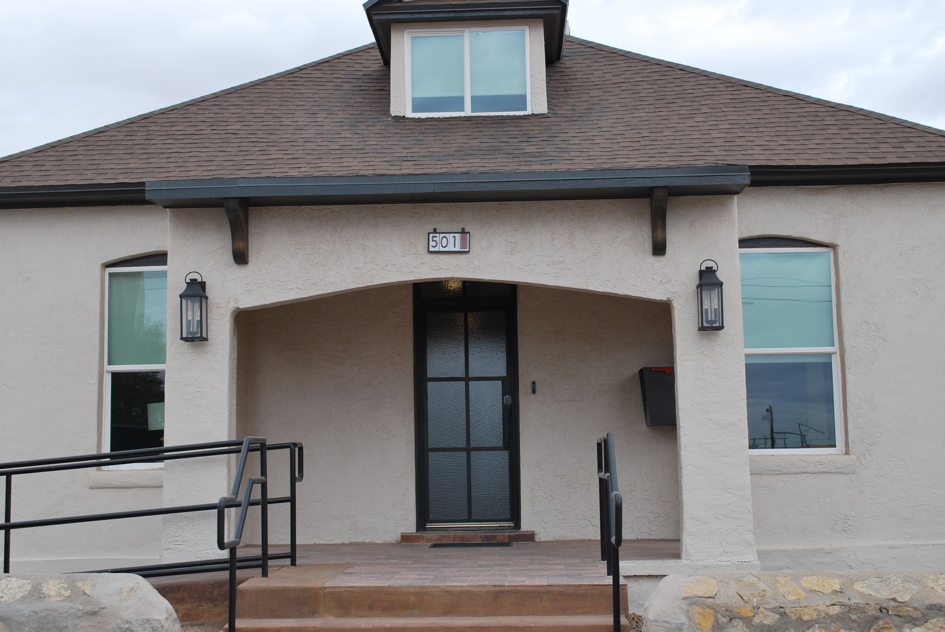 Tan house with a black door, two windows, and a black ramp leading to the entrance.