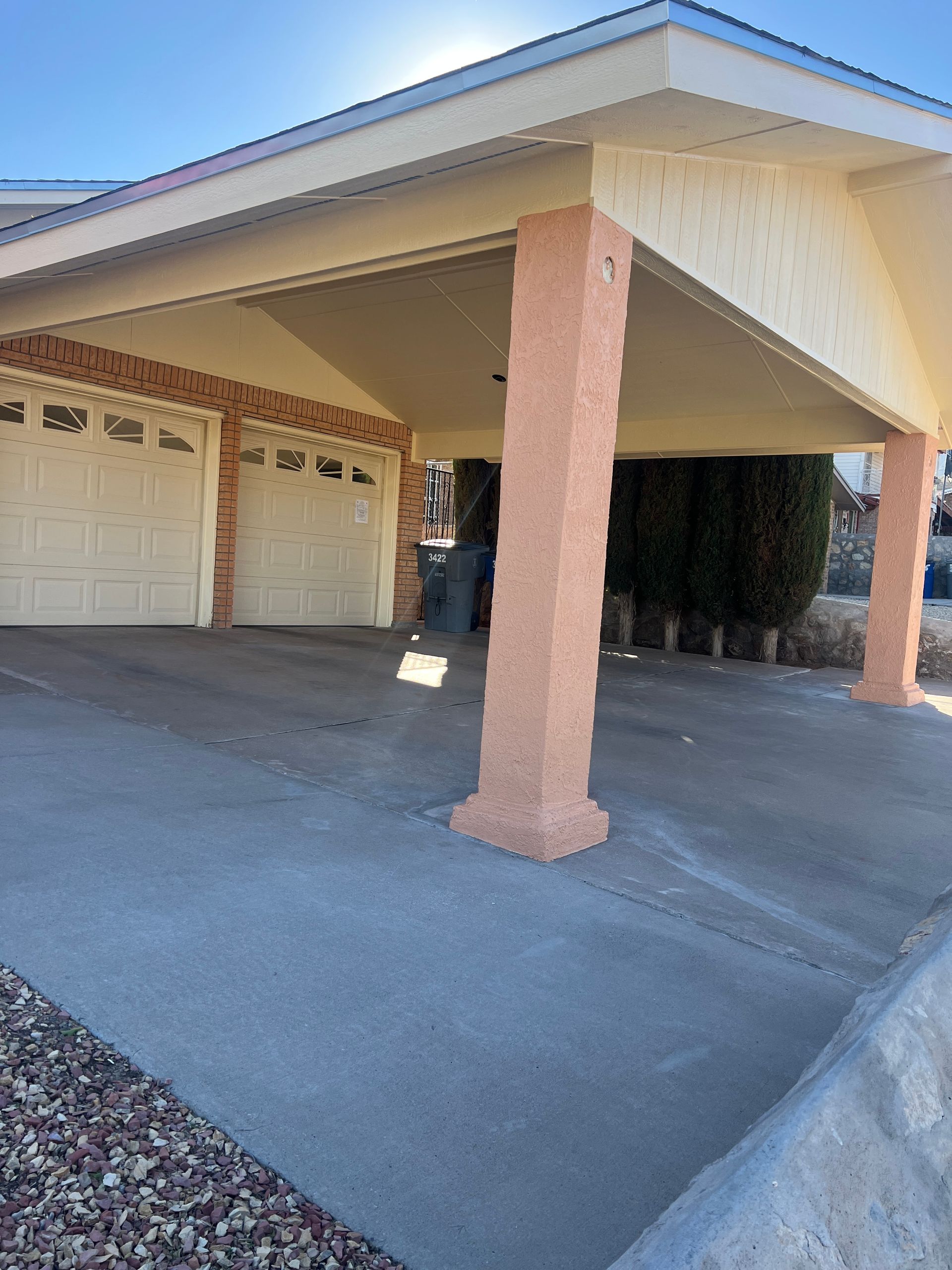 Carport with two garage doors and concrete driveway. Peach-colored support columns.