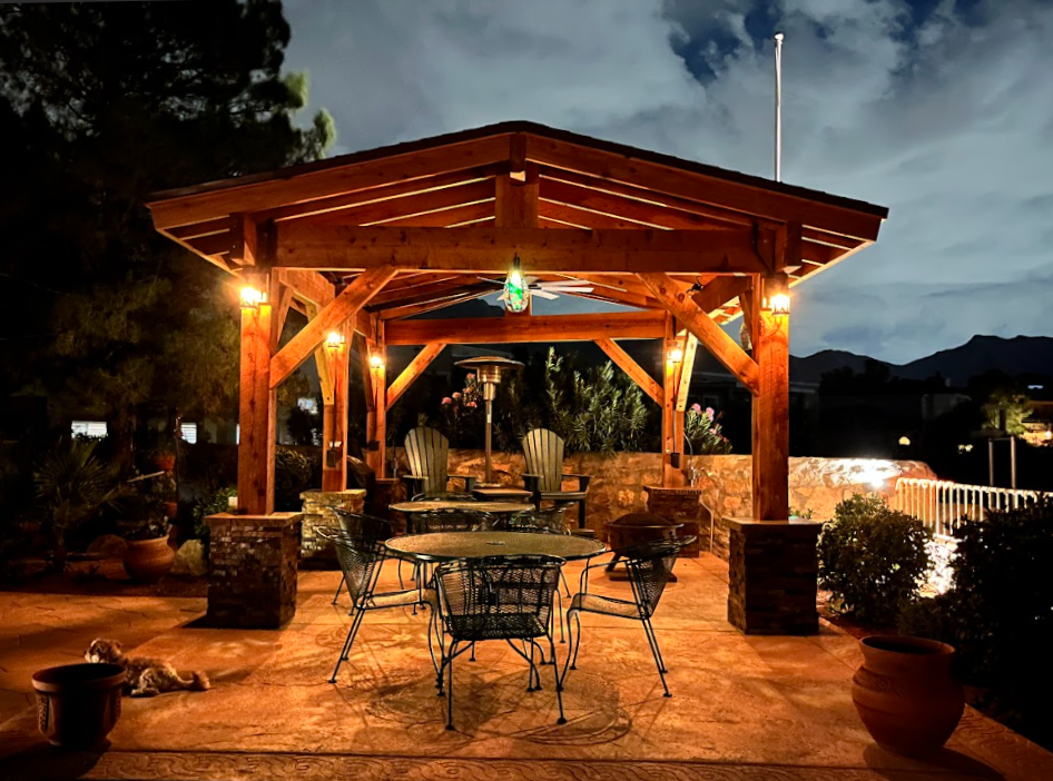 Wooden gazebo with tables, chairs, and heater, illuminated at night.