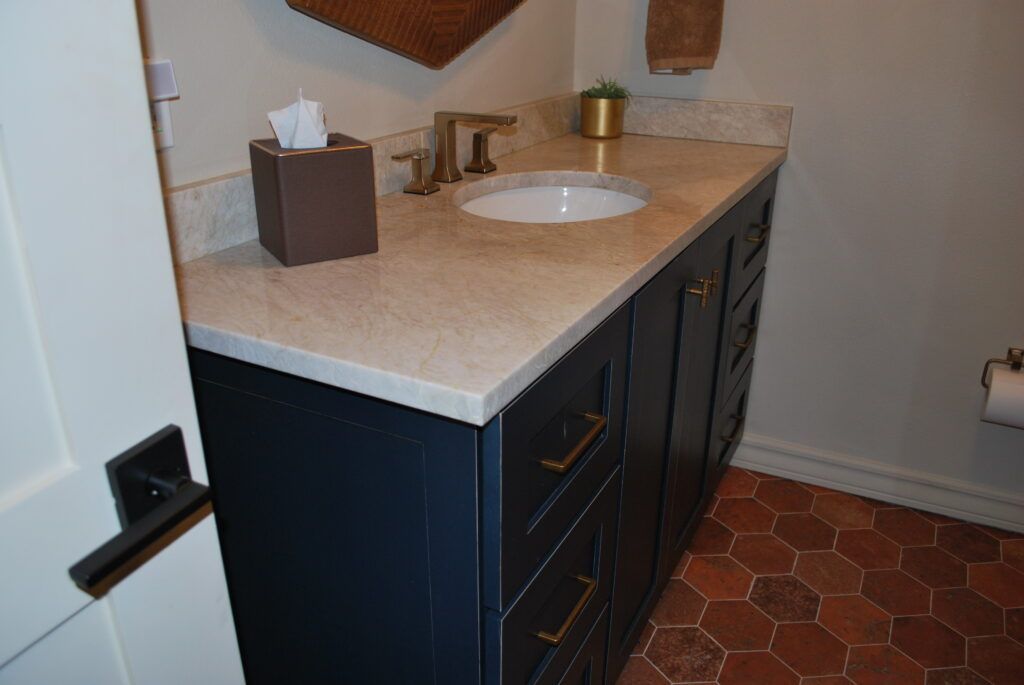 Dark blue bathroom vanity with gold hardware, light countertop, and red tile floor.