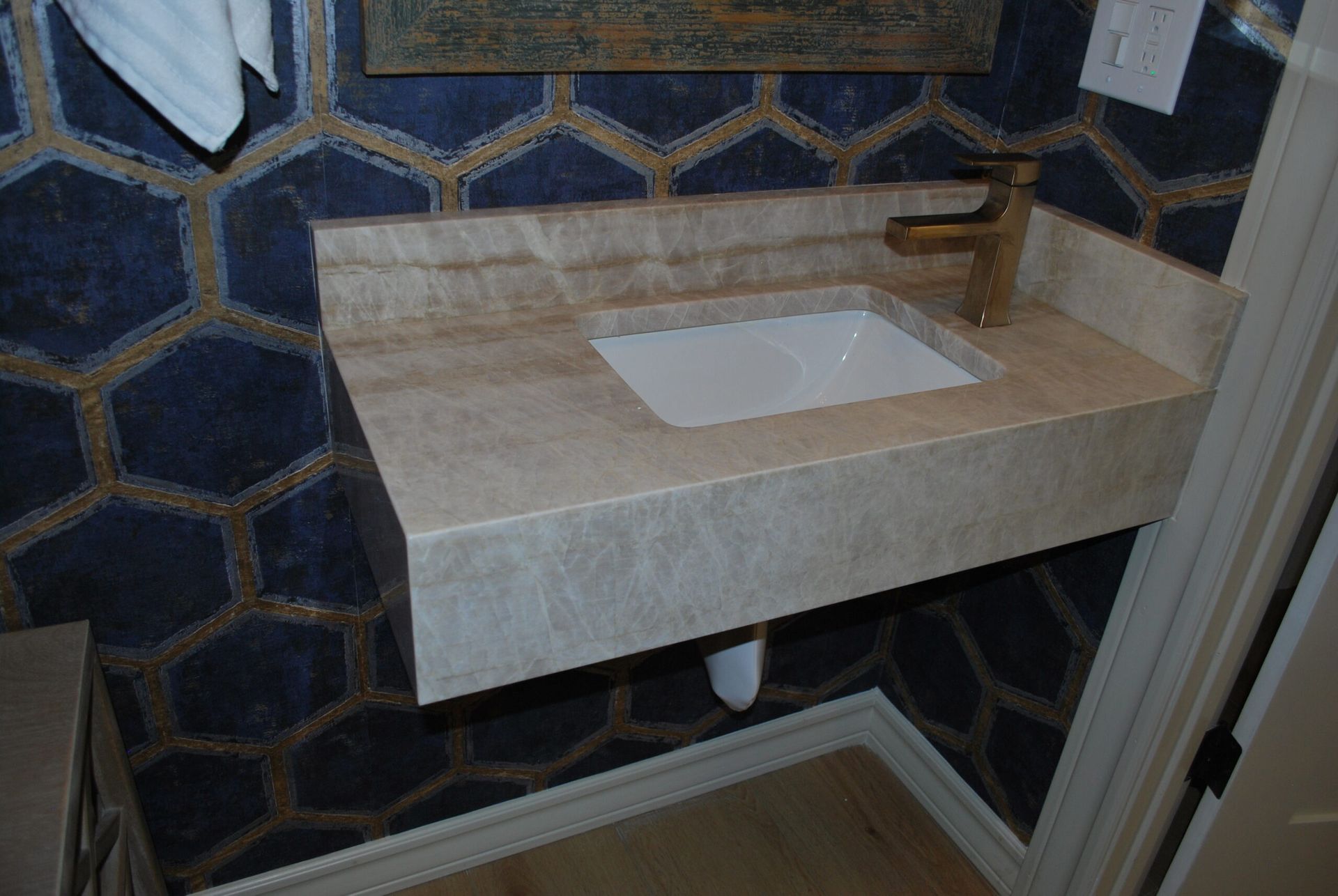 Floating stone vanity with gold faucet over a white sink, against a blue and gold honeycomb tile wall.
