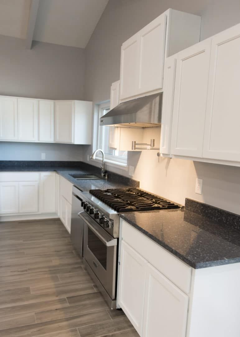 White kitchen with stainless steel appliances, dark countertops, and gray walls.