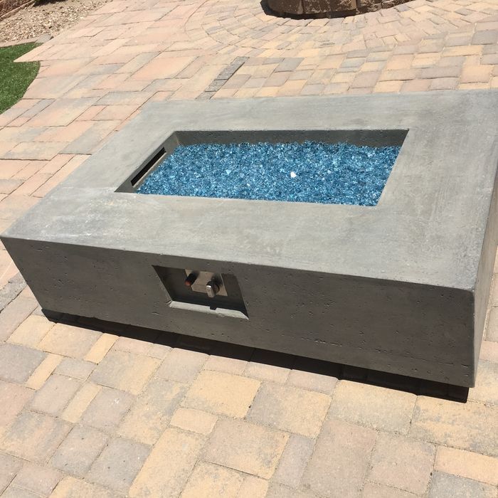 Concrete rectangular fire pit with blue glass, set on a stone patio.
