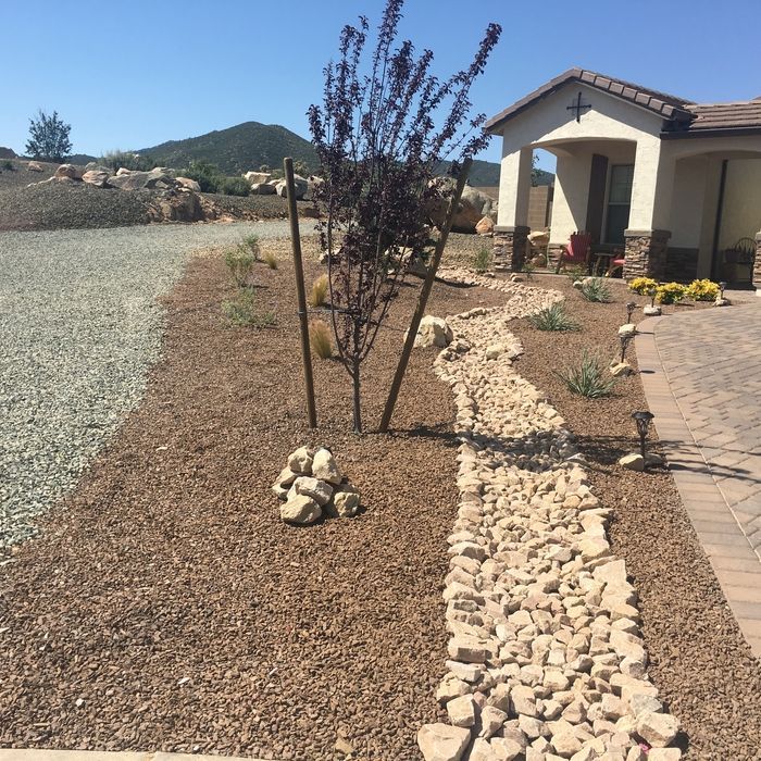 A house exterior with gravel landscaping, a dry creek bed, and a purple tree.