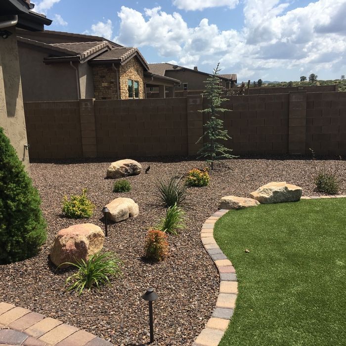Backyard landscaping with rocks, gravel, small plants, and a small patch of green turf.