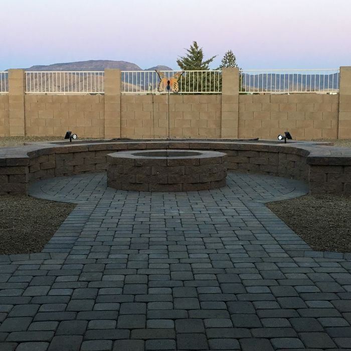 Brick patio with fire pit, tan retaining wall, white fence, mountains in background.