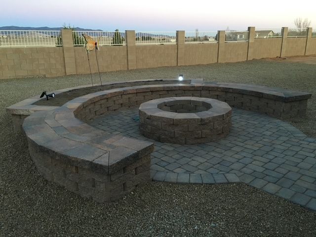 Brick fire pit with surrounding seating on a stone patio in a backyard with a fence.