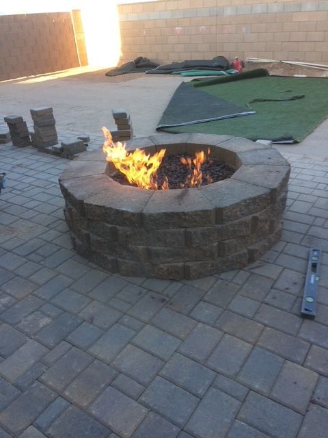 A fire pit with flames burning in a backyard patio. Bricks are in the background.