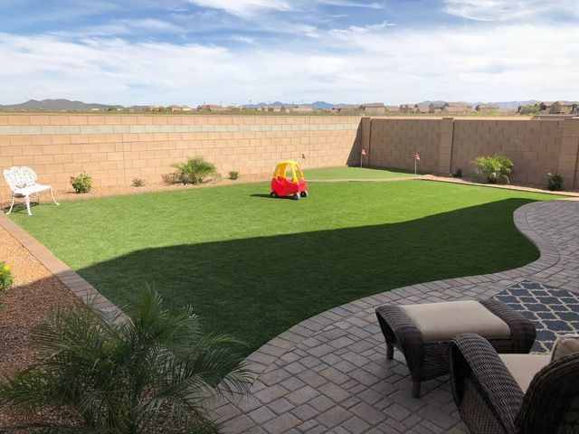 Lush green backyard with a brick patio, beige wall, and a child's toy car.
