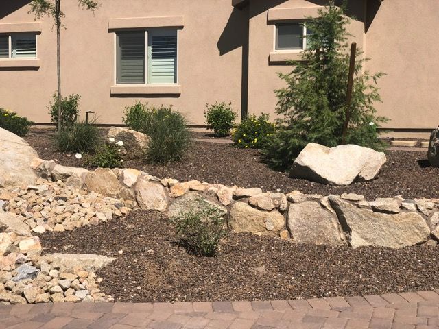 Rock wall and landscaping in front of a tan building with windows; gravel and plants.